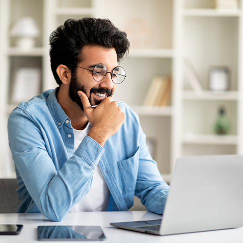 Smiling man sitting at desk looking at laptop
