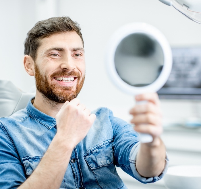 Man in dental chair admiring his smile in mirror after cosmetic dentistry in Wesley Chapel