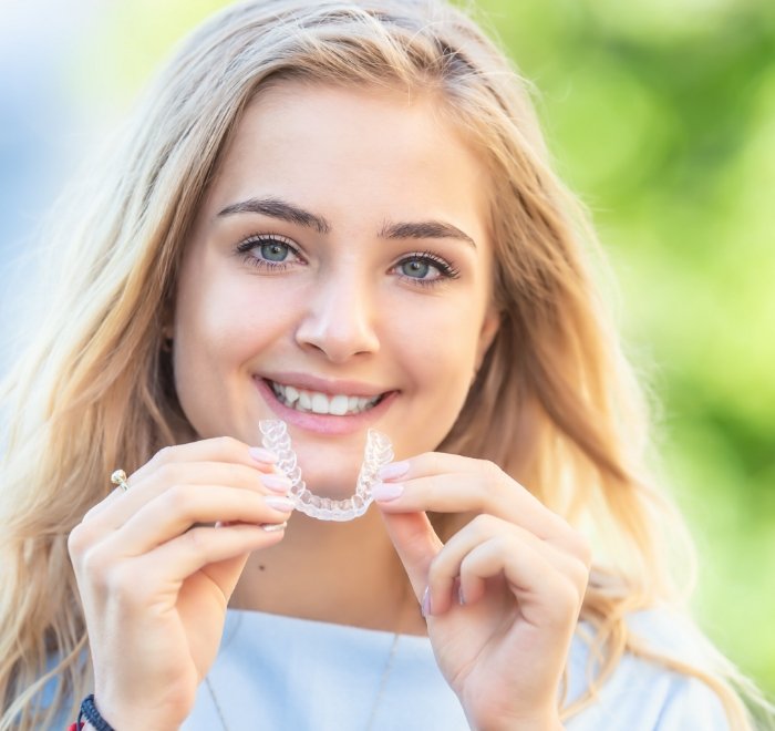 Smiling blonde woman holding an Invisalign clear aligner in Wesley Chapel