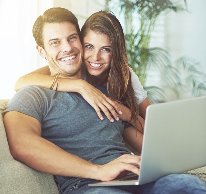 Smiling young man and woman sitting on couch and looking at laptop